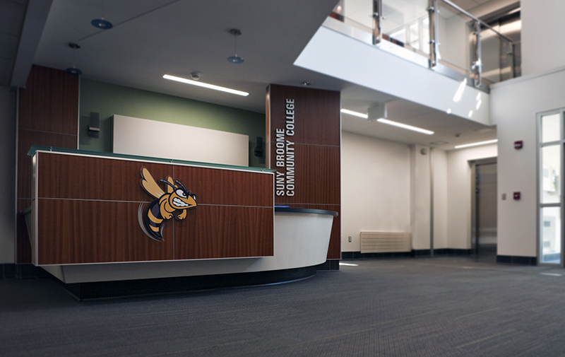 Interior image of lobby main desk featuring school hornet logo.